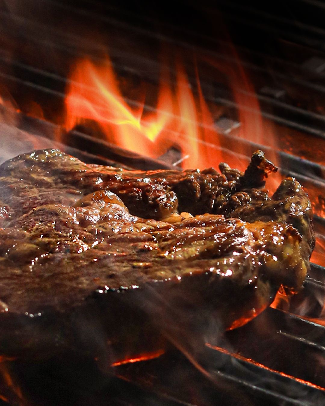 A thick cut of beef sizzling over flames